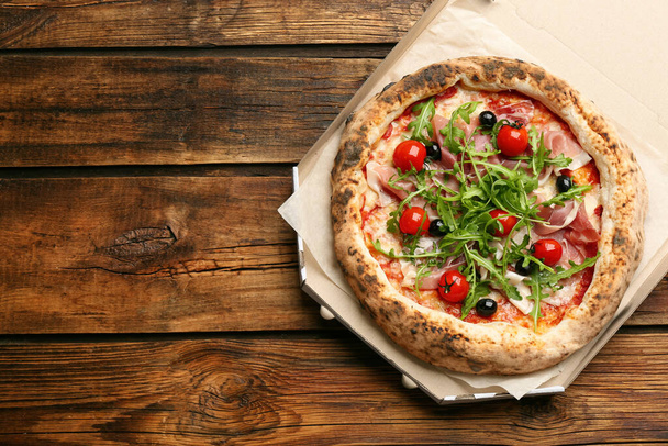 Tasty pizza with meat and arugula in cardboard box on wooden table, top view. Space for text - Foto, imagen
