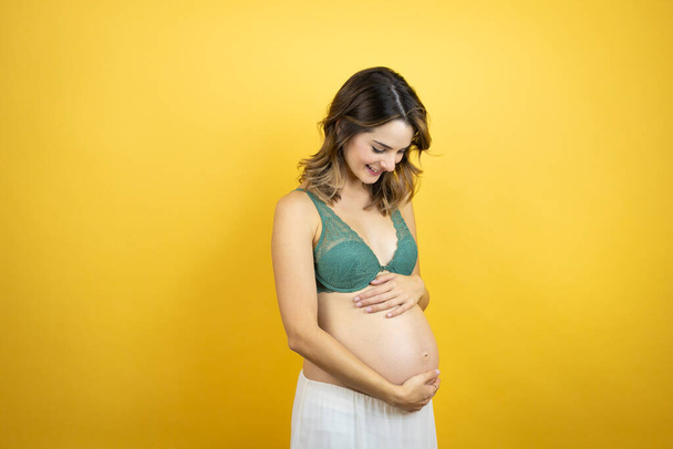 Fiatal gyönyörű barna nő terhes vár baba felett elszigetelt sárga háttér egy boldog arc áll, és mosolyog egy magabiztos mosoly mutatja fogak - Fotó, kép