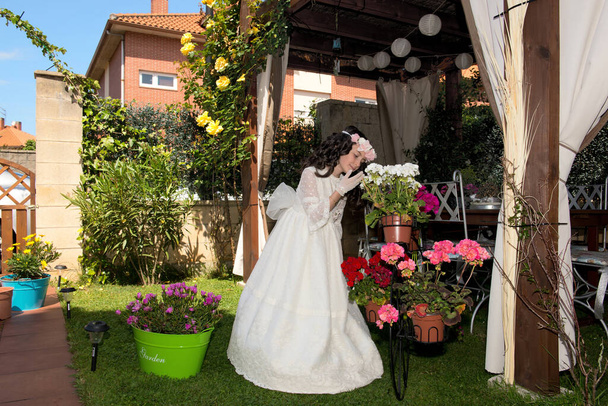 Niña vestida de primera comunion en jardín romantico con rosas y regadera en la mano - Foto, Imagen