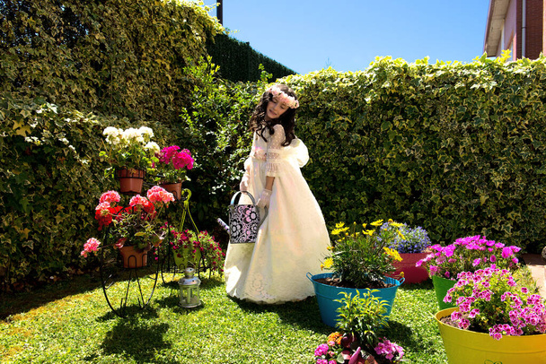Niña vestida de primera comunion en jardín romantico con rosas y regadera en la mano - Foto, Imagen