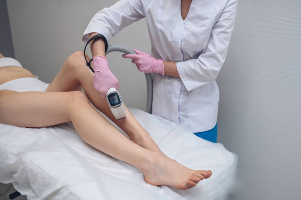 Laser epilation and cosmetology in beauty salon. Hair removal procedure. Laser epilation, cosmetology, spa, and hair removal concept. Beautiful blonde woman getting hair removing on legs - Photo, Image
