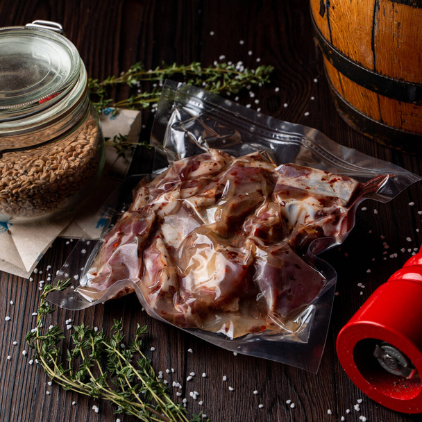Rohes mariniertes Fleisch in einer Vakuumverpackung auf einem dunklen Holztisch, Essenslieferung - Foto, Bild