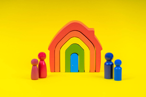 Dřevěné postavy, miniaturní lidé stojící před duhovým domem na žlutém pozadí. Rozvod, spor mezi rodiči, péče o děti po rozvodu - Fotografie, Obrázek