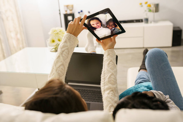 Две подруги делают селфи с цифровым планшетом, сидящим дома на диване. - Фото, изображение