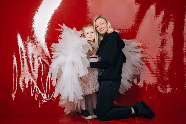 niña de 4 años con alas de ángel blanco sobre un fondo de látex rojo en el estudio para el día de San Valentín - Foto, Imagen