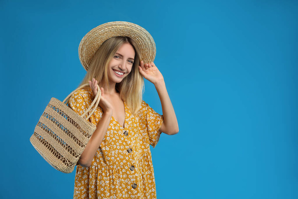Beautiful young woman with stylish straw bag on blue background. Space for text - Photo, Image