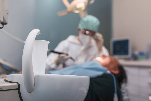 Glass of water in the dental office. Female doctor attending to a male patient. Focus on the white plastic cup. - 写真・画像