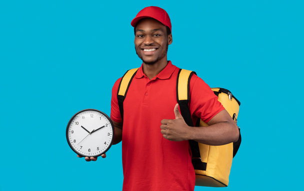Black delivery man holding clock showing thumb up - Photo, Image