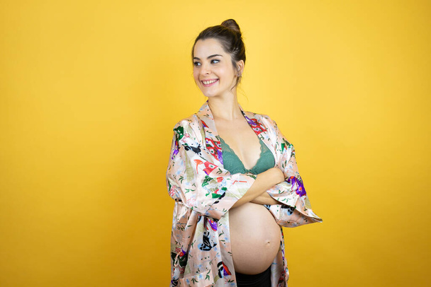 Nuori kaunis nainen raskaana odottaen vauvan yllään pyjama yli eristetty keltainen tausta etsii sivulle, rentoutua profiili aiheuttaa luonnolliset kasvot ja luottavainen hymy. - Valokuva, kuva