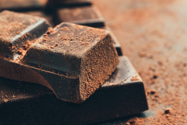 Chocolate bar and chopped chocolate cubes on dark background, close-up view. - 写真・画像