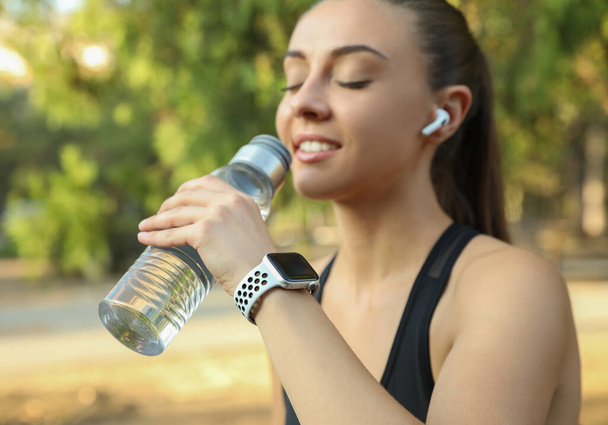 Woman with modern smart watch drinking water outdoors - Foto, Bild