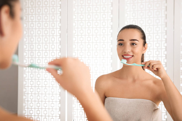 Woman brushing teeth in front of mirror at home - Foto, Imagem