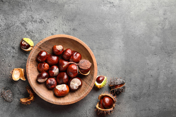 Horse chestnuts in wooden plate on grey table, flat lay. Space for text - Fotografie, Obrázek