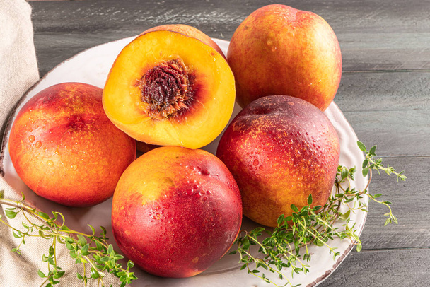Ripe peaches with thyme leaves in a plate on a wooden board on a background - Photo, Image