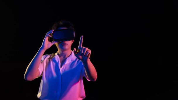 Jonge Aziatische man krijgt ervaring met VR virtual reality headset of 3D bril wijzen met zijn vinger op zwarte achtergrond. Donkere Toon. technologie, gaming, entertainment concept - Foto, afbeelding