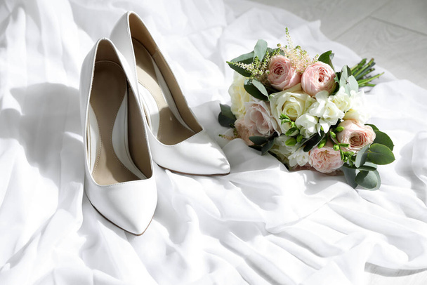 Pair of wedding high heel shoes and beautiful bouquet on white fabric - Valokuva, kuva
