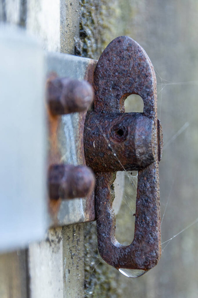 a close up view of a wet rusted slide lock on the side of a house box with a warer droplet at the bottom  - Photo, Image