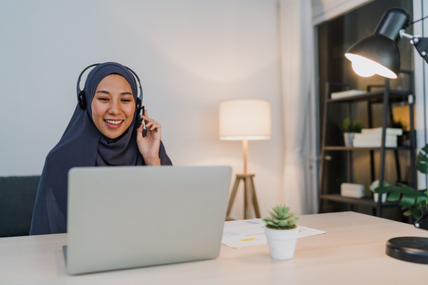 Asiens muslimische Dame trägt Kopfhörer Uhr Webinar hören Online-Kurs kommunizieren per Videokonferenz in der Nacht Home Office. Fernarbeit von zu Hause aus, soziale Distanz, Quarantäne für Coronavirus. - Foto, Bild