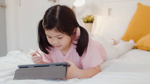 Young Asian girl drawing at home. Asia japanese woman child kid relax rest fun happy using tablet draw cartoon before sleep lying on bed, feel comfort and calm in bedroom at night concept. - Foto, Imagem