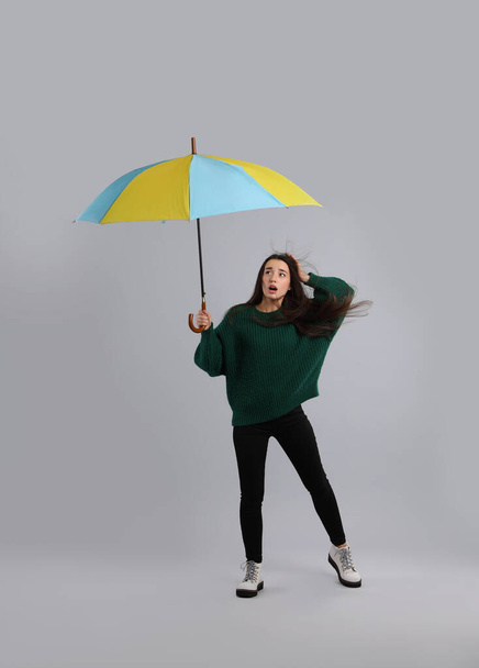 Emotional woman with umbrella caught in gust of wind on grey background - Фото, изображение
