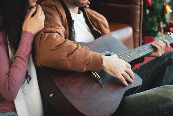Kaukasischer Freund spielt Gitarre mit Freundinnen im heimischen Wohnzimmer. Konzept miteinander verknüpfen - Foto, Bild