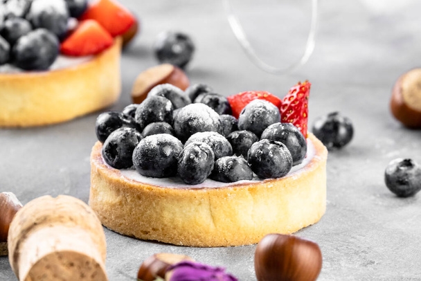 Blueberry and strawberry shortcake. There are hazelnuts, roses and wine corks on the table. Stone gray background. - Photo, Image