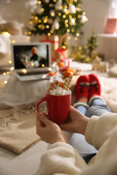 MYKOLAIV, UKRAINE - DECEMBER 25, 2020: Woman with sweet drink watching The Queen's Gambit series on laptop at home, closeup. Cozy winter holidays atmosphere - Foto, Imagem