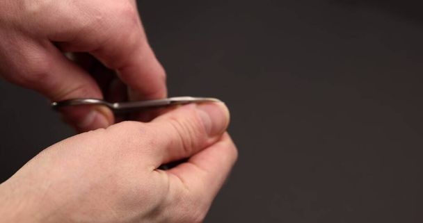 Man cuts fingernail for himself against dark background - Valokuva, kuva