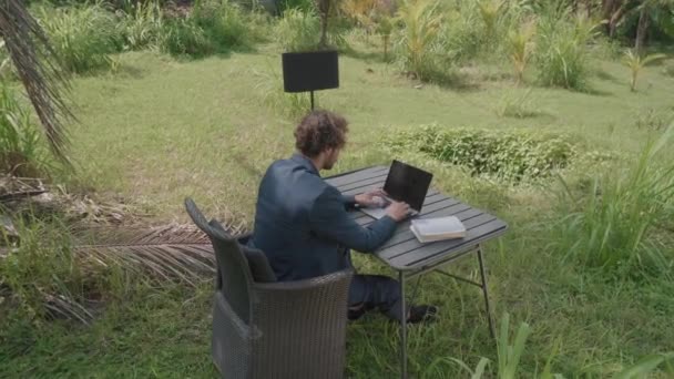 Korkean kulman taustakuvaa liikemiehestä, joka istuu työpöydän ääressä Balilla työskentelemässä kannettavan tietokoneen kanssa. - Materiaali, video