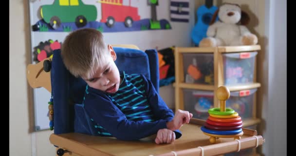 Actividades sensoriales para niños con discapacidad. Actividades preescolares para niños con necesidades especiales. Niño con parálisis cerebral en silla especial jugar y sonreír en casa. - Imágenes, Vídeo