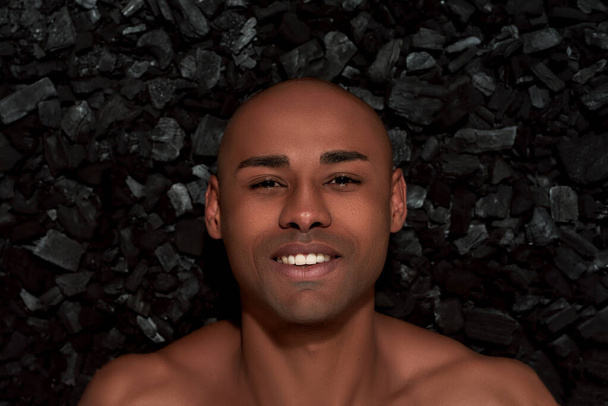 Close up portrait of handsome young african american man smiling at camera, posing isolated over black charcoal background - Fotó, kép