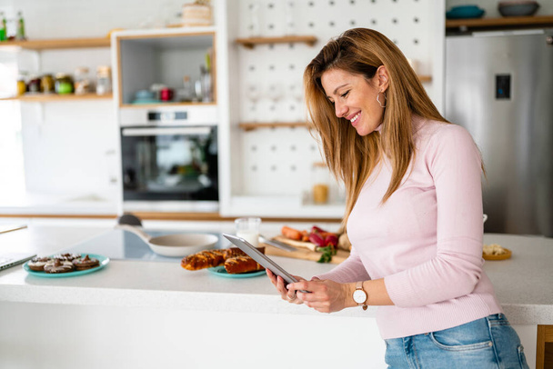 Smiling young woman with tablet in the kitchen. Technology, people concept - Valokuva, kuva