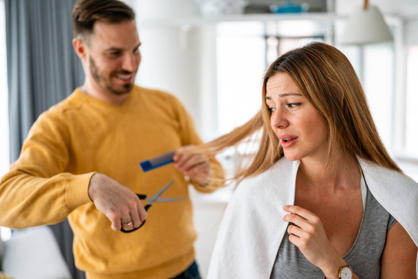 Man makes haircut to woman at home during quarantine. Isolation, couple, haircut concept. - Фото, зображення