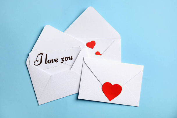 Card with phrase I Love You in envelope and red hearts on light blue background, flat lay - Foto, immagini