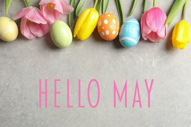 Merhaba May. Gri arka planda boyanmış Paskalya yumurtaları ve bahar çiçeklerinin düz kompozisyonu - Fotoğraf, Görsel