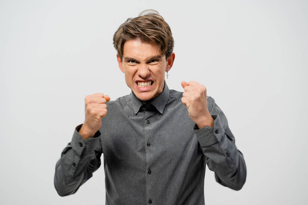 Ready to fight young man defending himself hands in fists in grey shirt with. Angry young adult man showing he is ready for fight isolated on white background - Foto, immagini