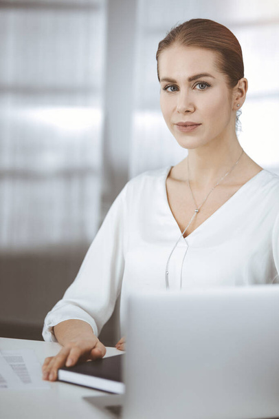 Businesswoman sitting and looking at camera in sunny office - Zdjęcie, obraz
