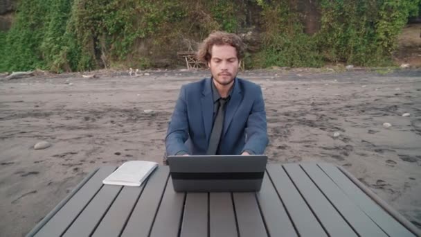 Handheld taille-up beelden van jonge Kaukasische zakenman werken op laptop in prachtige tropische bestemming - Video