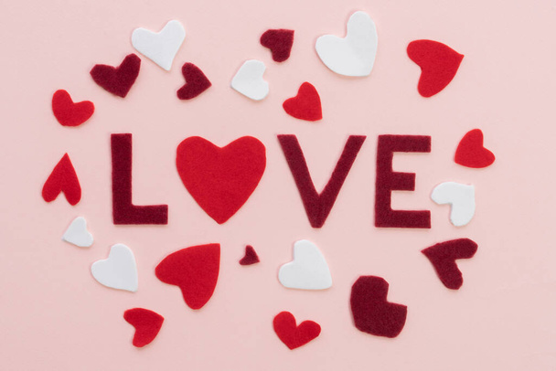Samenstelling voor Valentijnsdag 14 februari Zacht roze schattig achtergrond frame woord liefde, rood en wit harten gesneden uit vilt. Wenskaart plat lay top view 2021 Love concept. - Foto, afbeelding