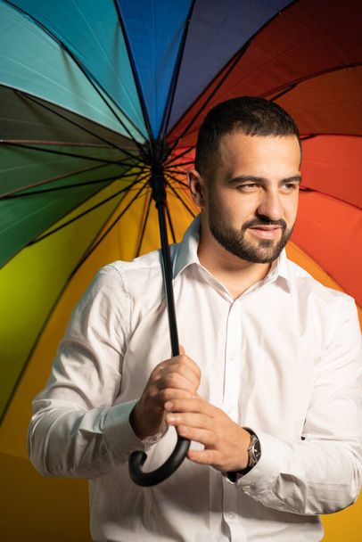 Supporting minorities straight handsome guy with a rainbow umbrella behind his back. Healthy fashion lifestyle, people sincere emotions, cold season concept. Handsome guy in support of LGBTQ society - Photo, Image