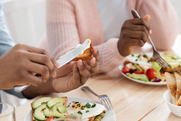 Petit déjeuner. Couple afro-américain méconnaissable appréciant la nourriture savoureuse dans la cuisine - Photo, image
