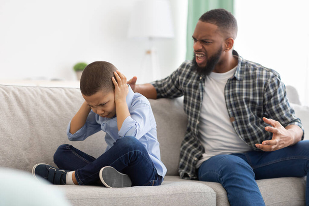 Θυμωμένος Αφρικανός πατέρας φωνάζει στο φοβισμένο γιο κάθεται στο σπίτι - Φωτογραφία, εικόνα
