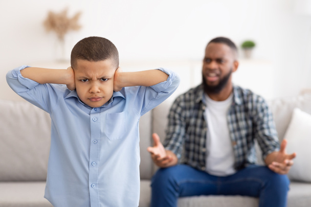 Μαύρο αγόρι καλύπτει αυτιά, ενώ θυμωμένος πατέρας φωνάζει στο σπίτι - Φωτογραφία, εικόνα