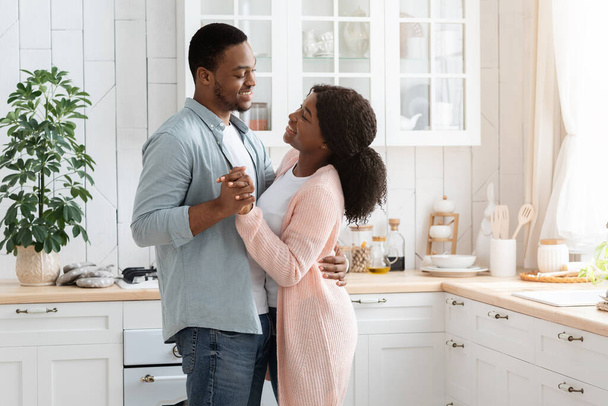 Ρομαντικό ζευγάρι στο σπίτι. Αγαπώντας African American Σύζυγοι Χορεύοντας στο εσωτερικό της κουζίνας - Φωτογραφία, εικόνα