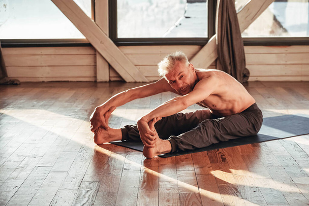 Hombre mayor con un torso desnudo practicando yoga clásico de asana entrenándose en estudio frente a una ventana. Copiar, espacio vacío para texto. - Foto, imagen