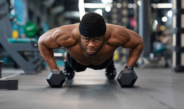 Confident black guy sportsman pushing up with dumbbells - Foto, Imagem