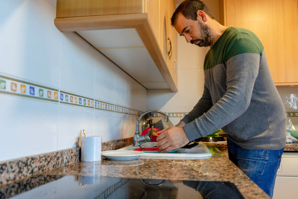 Бородатий чоловік миє посуд на своїй домашній кухні. Концепція доглядача
 - Фото, зображення