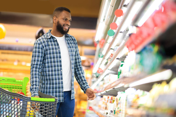 afro-americano cara compra comida de pé perto prateleira no supermercado - Foto, Imagem