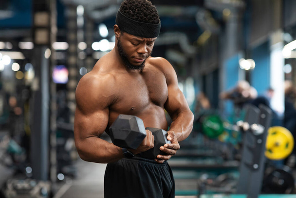 Koncentrált fekete sportoló edzés karok súlyzókkal a tornateremben - Fotó, kép
