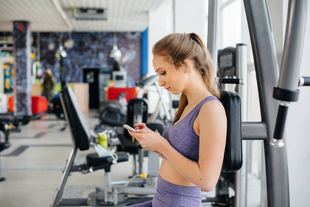 A young athlete uses her phone in the gym and takes a selfie. - Foto, Bild